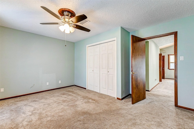 unfurnished bedroom with ceiling fan, light colored carpet, a closet, and a textured ceiling