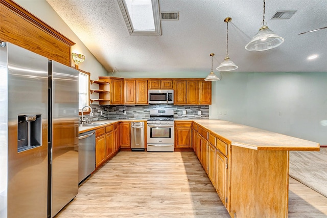 kitchen with lofted ceiling, sink, stainless steel appliances, decorative light fixtures, and light wood-type flooring