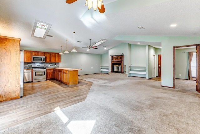 kitchen with lofted ceiling, ceiling fan, appliances with stainless steel finishes, hanging light fixtures, and kitchen peninsula