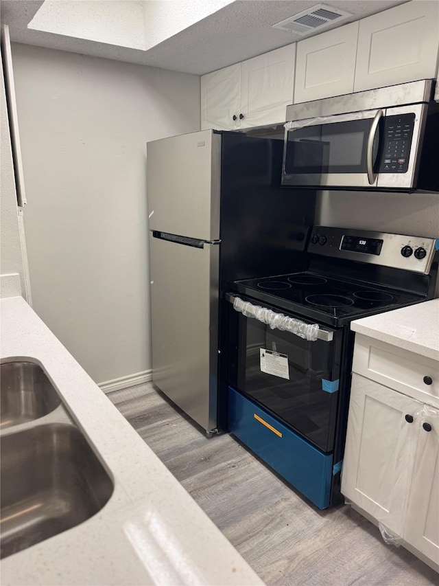 kitchen featuring range with electric stovetop, sink, white cabinets, and light wood-type flooring