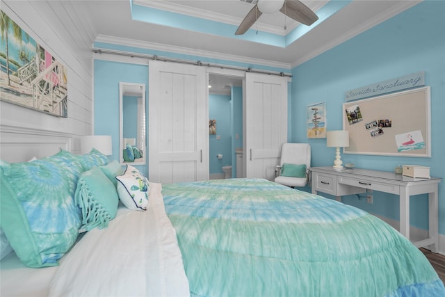 bedroom featuring wood-type flooring, ceiling fan, a raised ceiling, crown molding, and a barn door