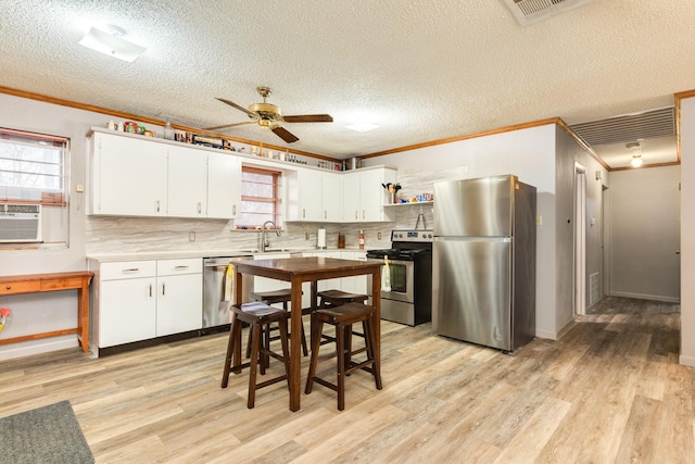 kitchen featuring crown molding, light hardwood / wood-style flooring, appliances with stainless steel finishes, backsplash, and white cabinets