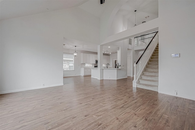 unfurnished living room with high vaulted ceiling, sink, and light hardwood / wood-style floors