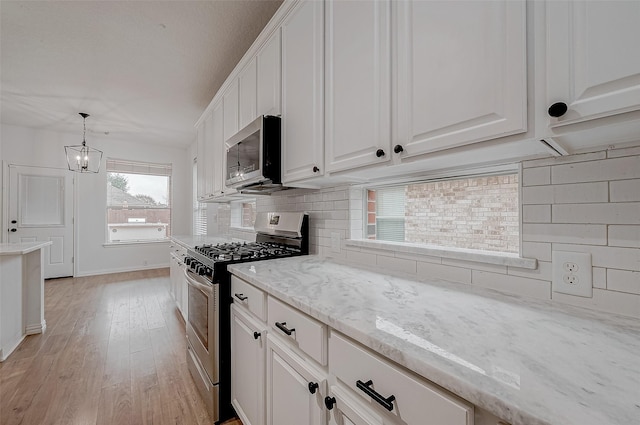 kitchen featuring appliances with stainless steel finishes, white cabinets, backsplash, and decorative light fixtures