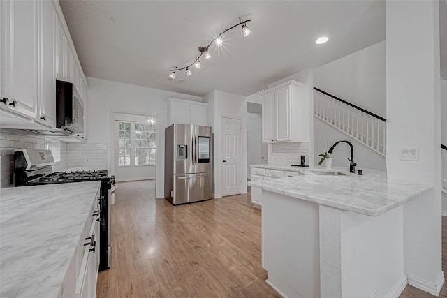 kitchen with appliances with stainless steel finishes, sink, white cabinets, kitchen peninsula, and light wood-type flooring