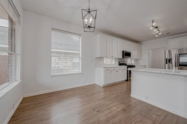 kitchen with white cabinetry, tasteful backsplash, decorative light fixtures, light hardwood / wood-style flooring, and appliances with stainless steel finishes