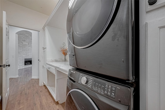 laundry room with stacked washer and dryer, a stone fireplace, and light hardwood / wood-style floors