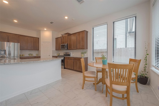 kitchen featuring appliances with stainless steel finishes, light stone countertops, sink, and backsplash