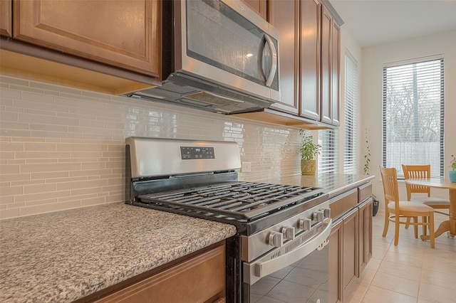 kitchen featuring tasteful backsplash, appliances with stainless steel finishes, light stone countertops, and light tile patterned floors