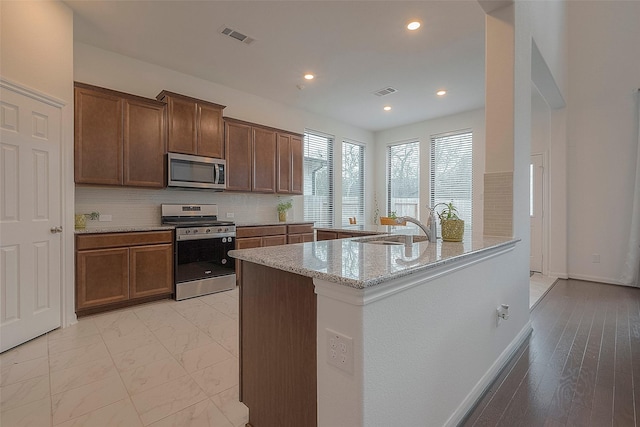 kitchen with light stone counters, stainless steel appliances, sink, and backsplash