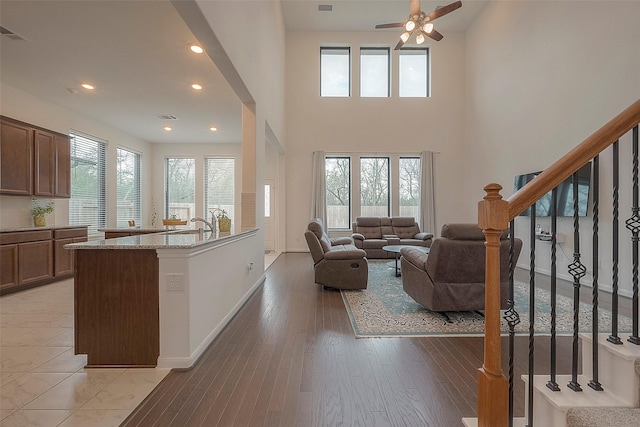 living room with sink, a towering ceiling, light hardwood / wood-style flooring, and ceiling fan