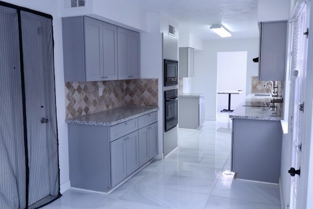 kitchen featuring light stone counters, gray cabinets, decorative backsplash, and black appliances