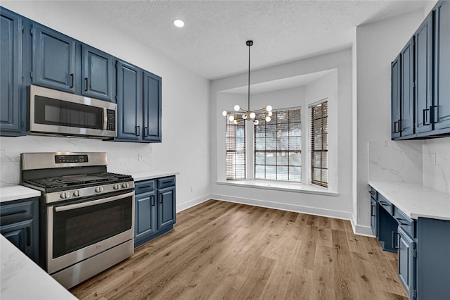 kitchen featuring appliances with stainless steel finishes, decorative light fixtures, blue cabinets, tasteful backsplash, and light wood-type flooring