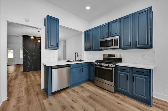 kitchen with blue cabinets, appliances with stainless steel finishes, sink, and light hardwood / wood-style floors