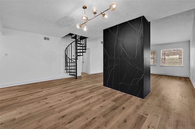 unfurnished living room with hardwood / wood-style flooring, an inviting chandelier, and a textured ceiling