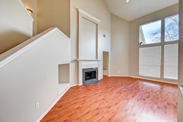 unfurnished living room featuring hardwood / wood-style floors, high vaulted ceiling, and a premium fireplace