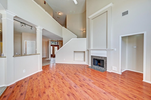 unfurnished living room with ornate columns, a high end fireplace, light wood-type flooring, and a towering ceiling