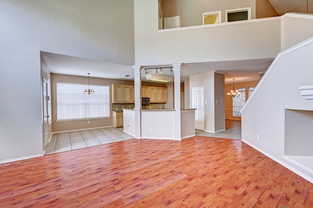 unfurnished living room with ornate columns, a towering ceiling, light wood-type flooring, and a notable chandelier