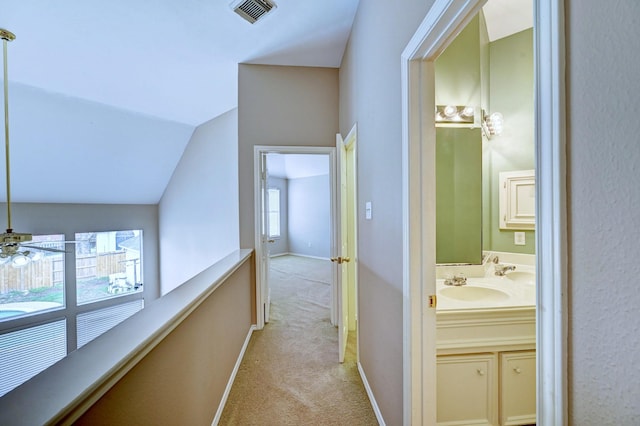 hallway featuring sink, vaulted ceiling, and light colored carpet