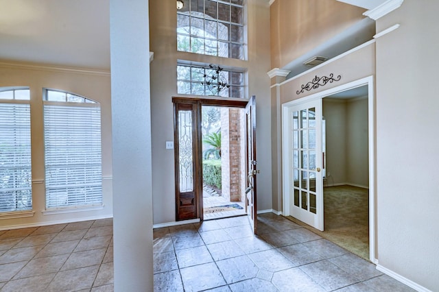 entrance foyer with light tile patterned flooring, ornamental molding, decorative columns, and a high ceiling