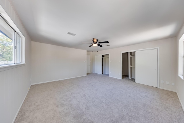 unfurnished bedroom with ceiling fan, light carpet, and two closets