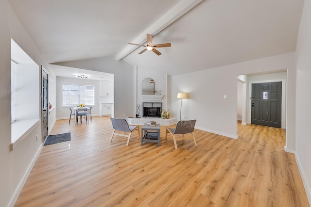 living room featuring a brick fireplace, lofted ceiling with beams, ceiling fan, and light wood-type flooring