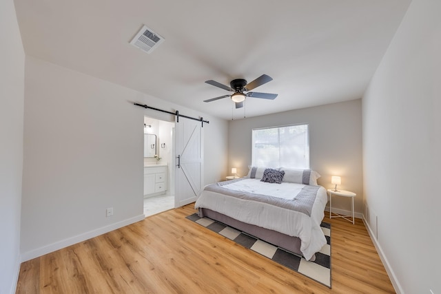 bedroom with ceiling fan, ensuite bath, a barn door, and light wood-type flooring