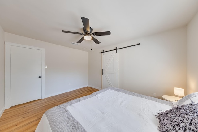 bedroom with hardwood / wood-style flooring, a barn door, and ceiling fan