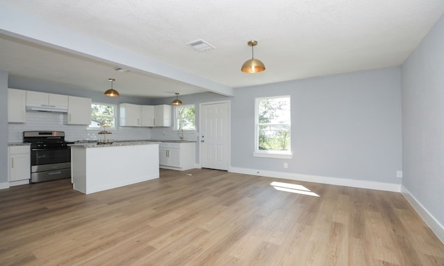 kitchen with a kitchen island, decorative light fixtures, white cabinetry, gas stove, and light stone countertops