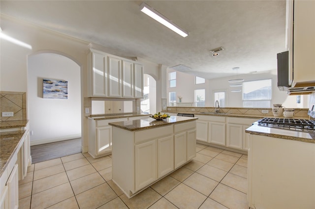 kitchen featuring light tile patterned floors, sink, stone counters, white cabinetry, and a center island