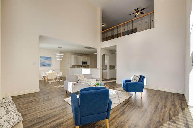 living room featuring ceiling fan, a towering ceiling, and dark hardwood / wood-style flooring