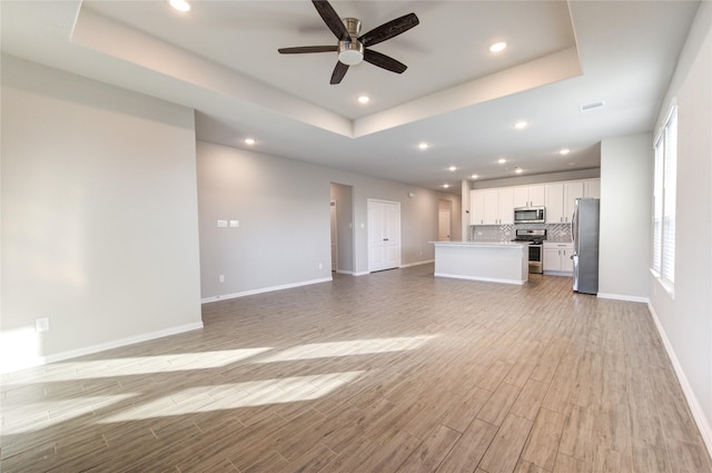 unfurnished living room featuring a tray ceiling, light hardwood / wood-style flooring, and ceiling fan