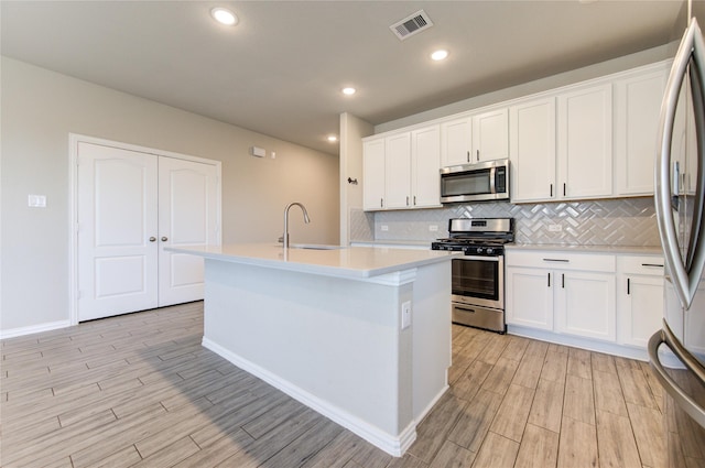 kitchen featuring sink, appliances with stainless steel finishes, tasteful backsplash, white cabinets, and a center island with sink