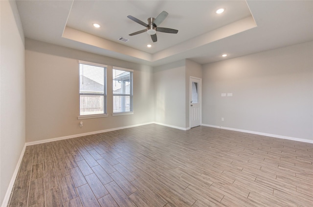 spare room with a raised ceiling, ceiling fan, and light hardwood / wood-style flooring