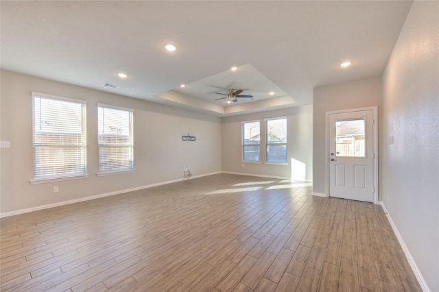 empty room with a raised ceiling, ceiling fan, and light hardwood / wood-style flooring