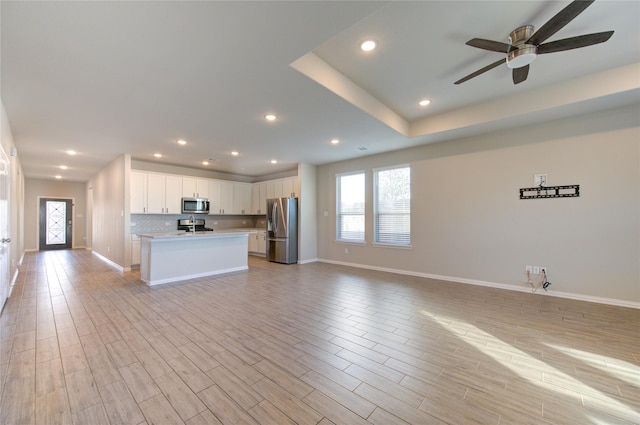 kitchen featuring white cabinetry, backsplash, a kitchen island with sink, stainless steel appliances, and light wood-type flooring