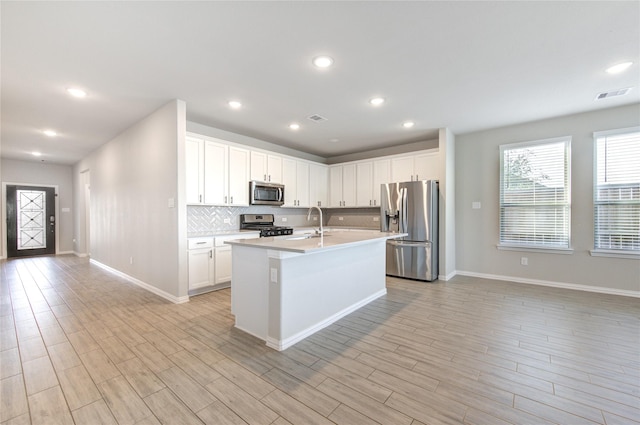 kitchen with white cabinetry, light wood-type flooring, appliances with stainless steel finishes, an island with sink, and backsplash