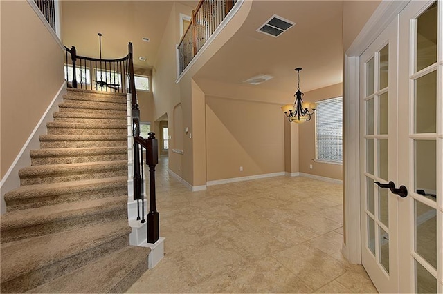 staircase featuring a high ceiling, a chandelier, and french doors