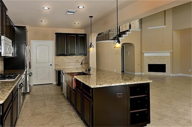 kitchen featuring appliances with stainless steel finishes, hanging light fixtures, dark brown cabinets, light stone counters, and a fireplace