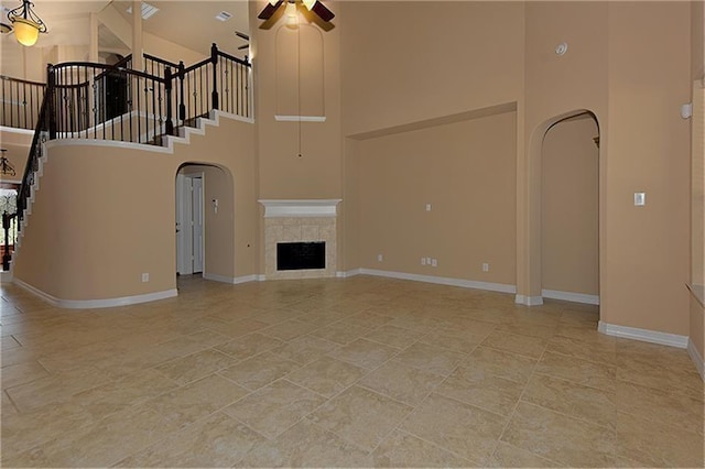 unfurnished living room featuring ceiling fan, a tile fireplace, and a high ceiling