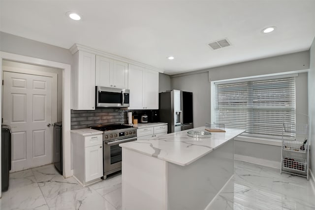 kitchen with appliances with stainless steel finishes, white cabinetry, backsplash, a center island, and light stone counters