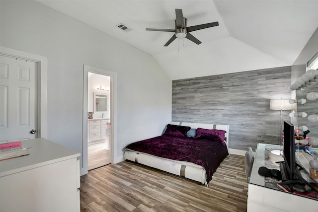 bedroom with lofted ceiling, ceiling fan, hardwood / wood-style floors, wooden walls, and connected bathroom