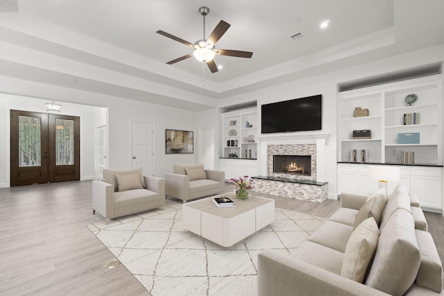 living room featuring light hardwood / wood-style flooring, a tray ceiling, a fireplace, built in shelves, and french doors