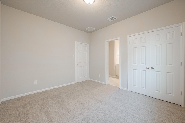 unfurnished bedroom featuring light colored carpet, ensuite bath, a closet, and a textured ceiling