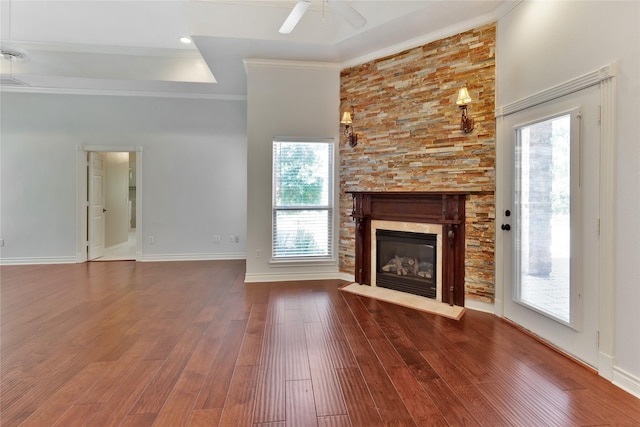 unfurnished living room with hardwood / wood-style flooring, a stone fireplace, a raised ceiling, and crown molding