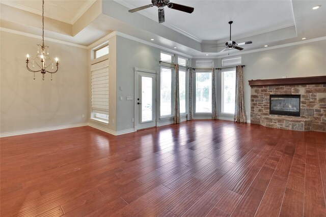 unfurnished living room featuring ceiling fan with notable chandelier, a fireplace, a tray ceiling, and hardwood / wood-style floors