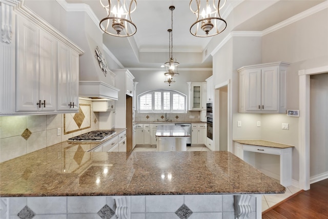 kitchen featuring white cabinetry, hanging light fixtures, appliances with stainless steel finishes, a raised ceiling, and stone counters