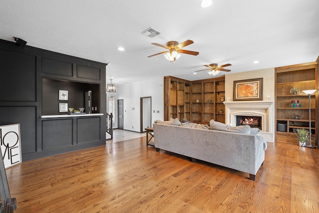 living room with ceiling fan, a textured ceiling, built in features, and light wood-type flooring