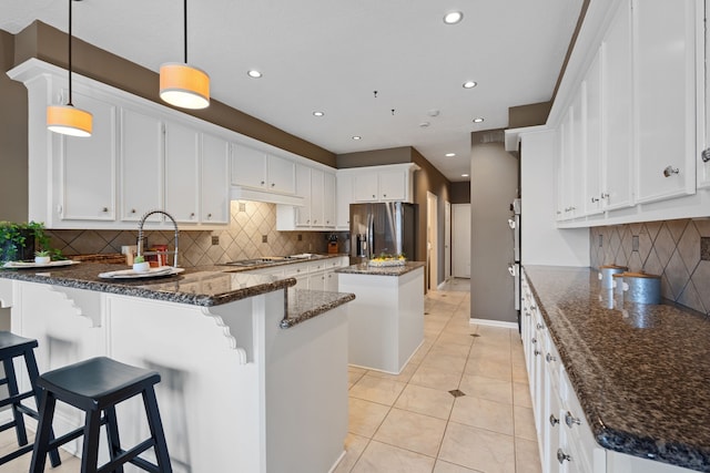 kitchen featuring white cabinetry, hanging light fixtures, stainless steel appliances, a kitchen island, and dark stone counters