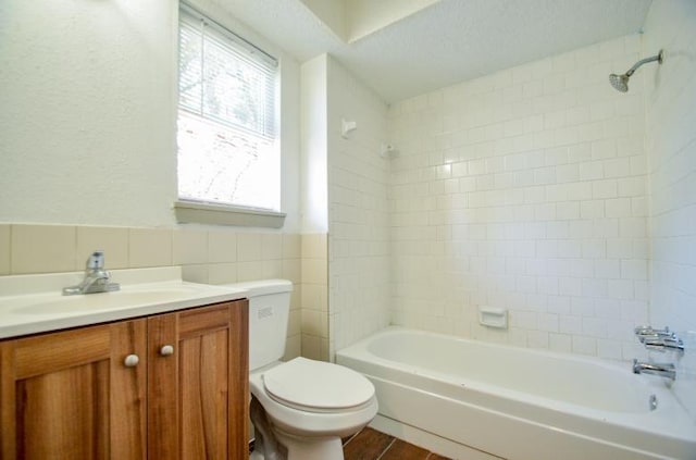 full bathroom featuring toilet, tile walls, a textured ceiling, vanity, and tiled shower / bath combo